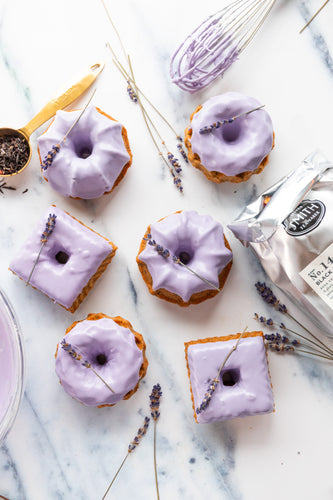 Several black lavender bundt cakes with purple icing on marble counter top.