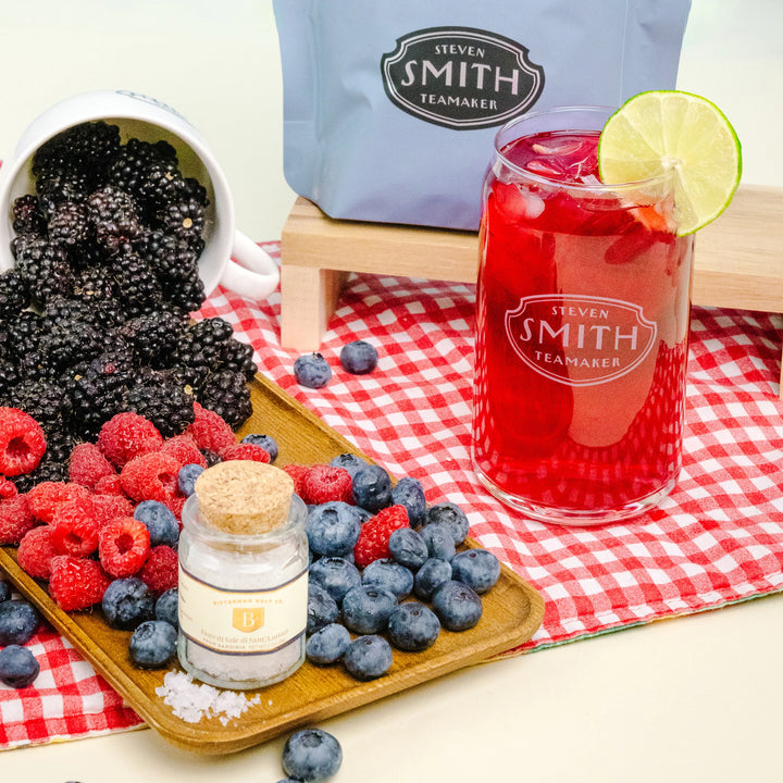 Lime Bramble-Ade beverage in a Smith branded can glass on a table with berries and jar of Bitterman salt.