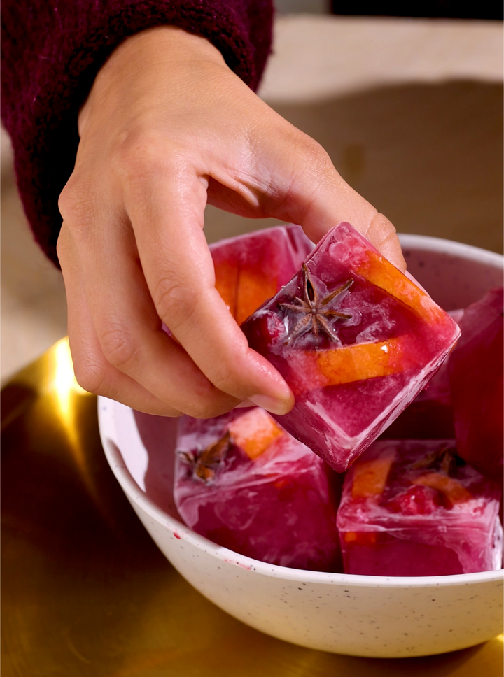 Up close of red Merry Maker's ice cubes with cranberries and orange peel within ice cube.