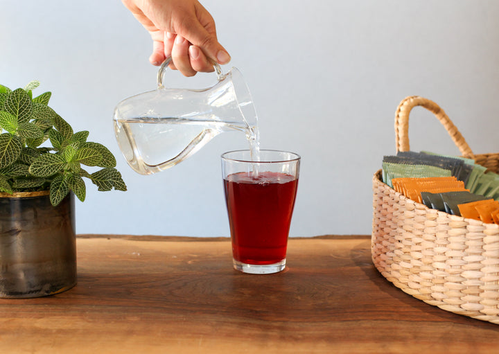 Hand pouring water into a glass of iced tea.