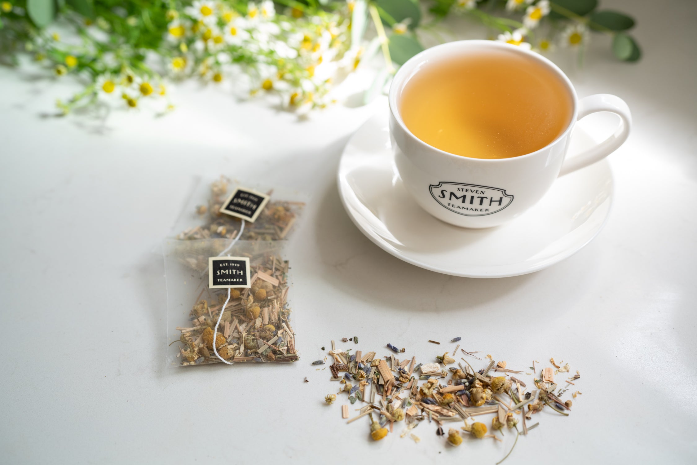 Unwrapped sachets of Lullaby and pile of loose blend beside a teacup filled with tea.