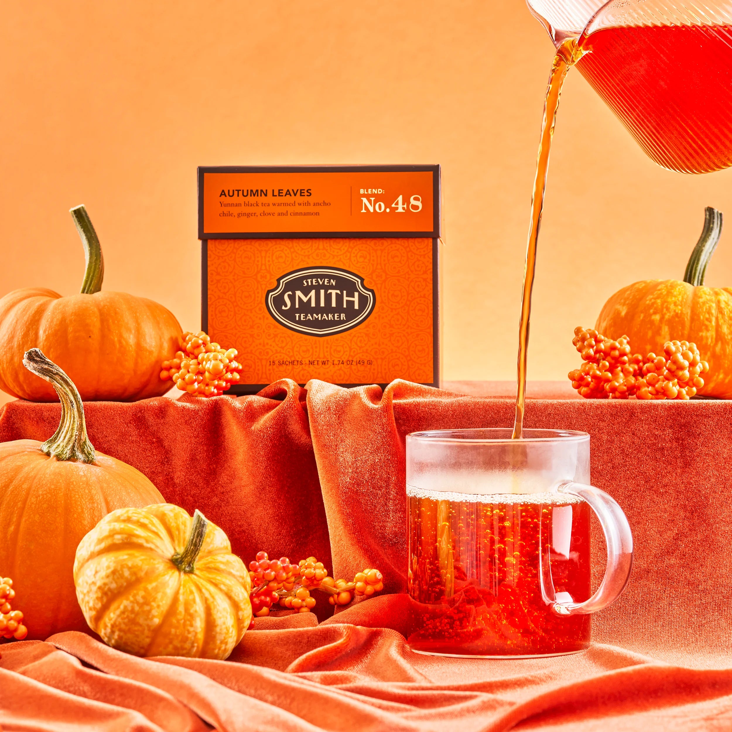 Deep orange box of Autumn Leaves surrounded by pumpkins with a teapot pouring tea into a clear mug.