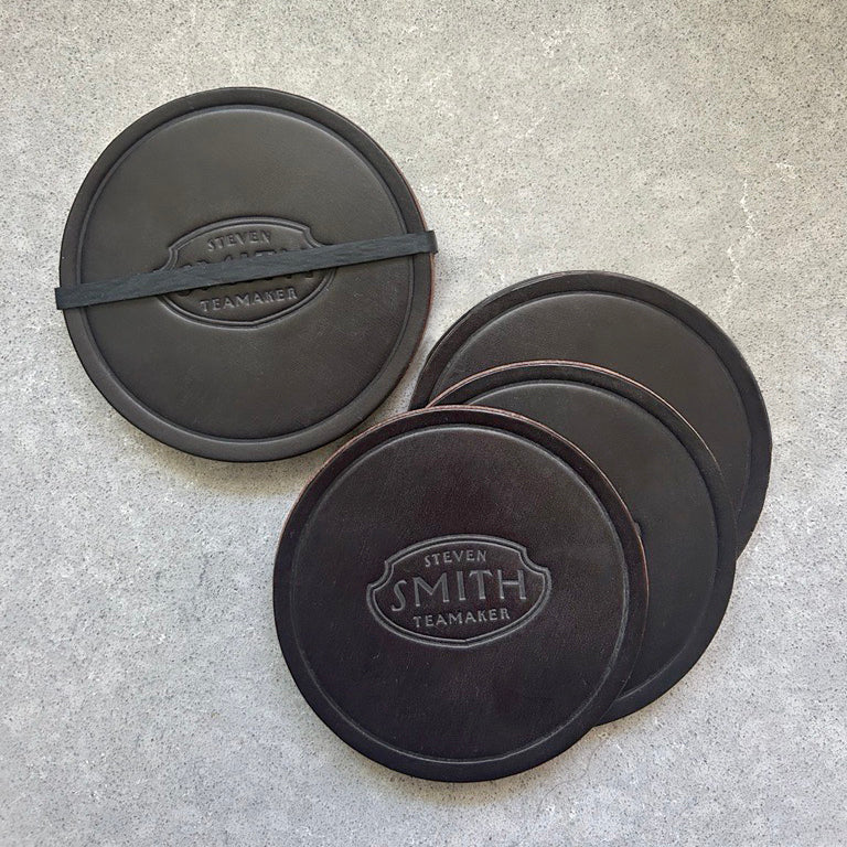 4 brown leather coasters branded with Steven Smith Teamaker on grey background