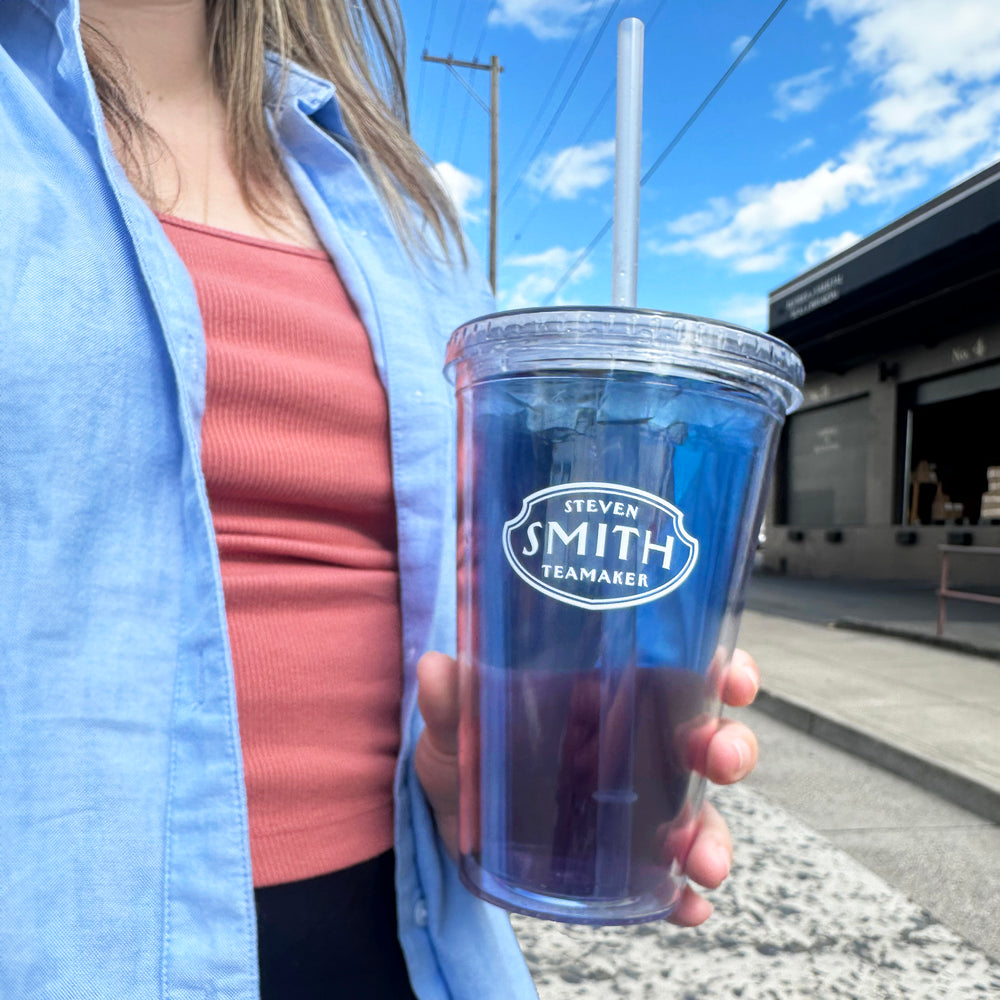 Clear cold cup filled with Blackberry Jasmine Iced Tea held by a person with a red shirt.