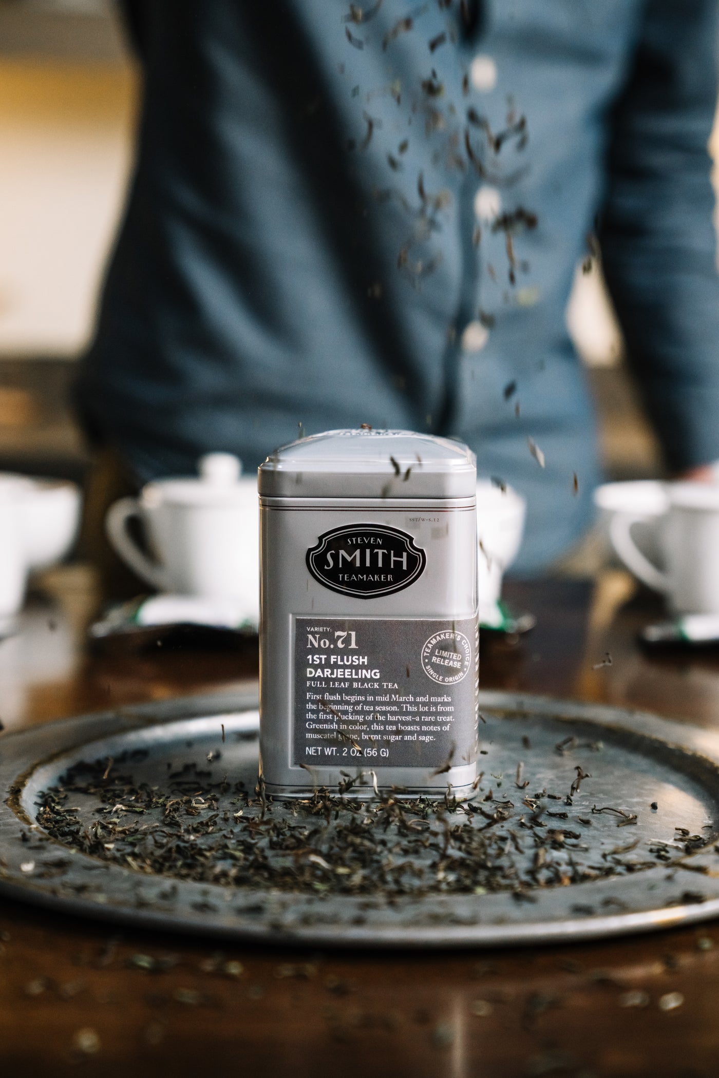 Tin of Darjeeling First Flush Teamaker's Choice on a silver plate with loose tea surrounding.