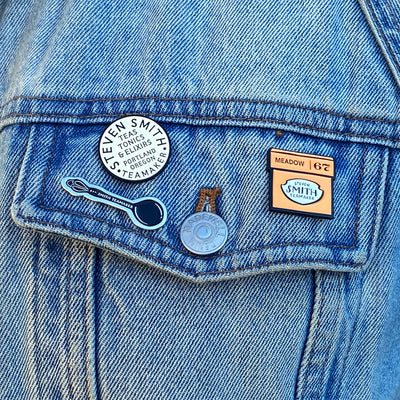 Tasting Spoon, Smith Seal and Meadow Carton enamel pins pinned to a denim jacket.