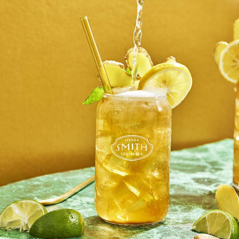 Glass of Ginger Splash Iced Tea with a straw and lemon and ginger garnish on a green marble counter.