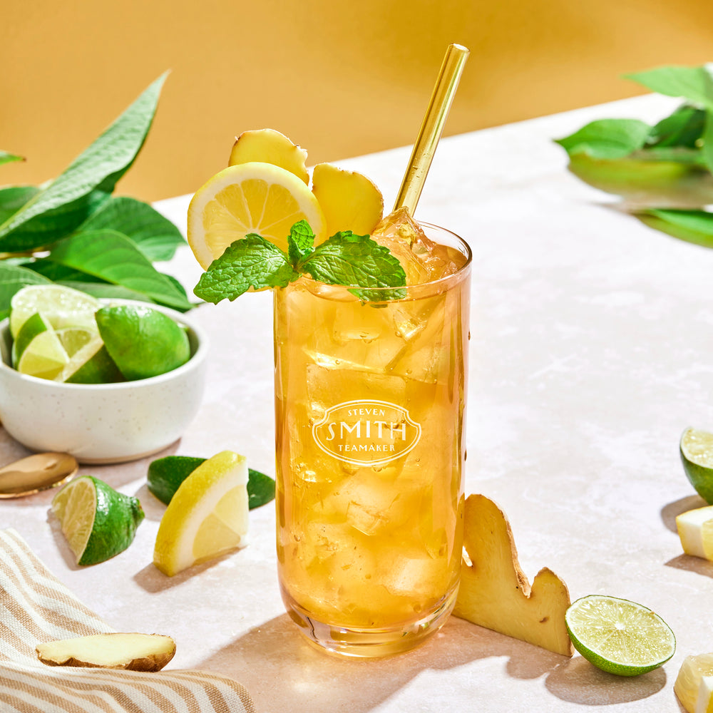 Glass of Ginger Splash Iced tea with a straw and lemon, ginger and mint garnish on a marble countertop.