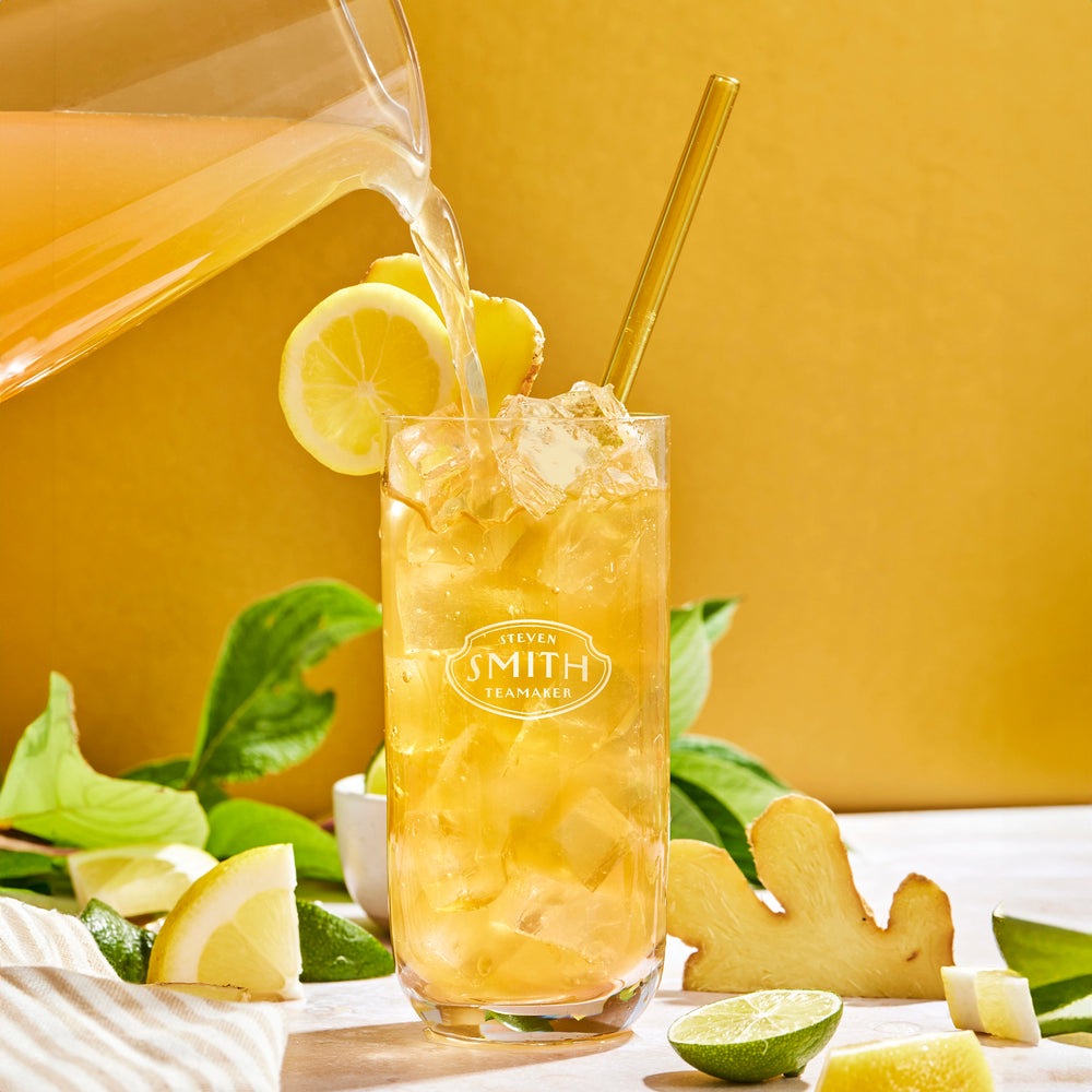 Pitcher pouring Ginger Splash Iced Tea into a glass garnished with lemon and ginger.