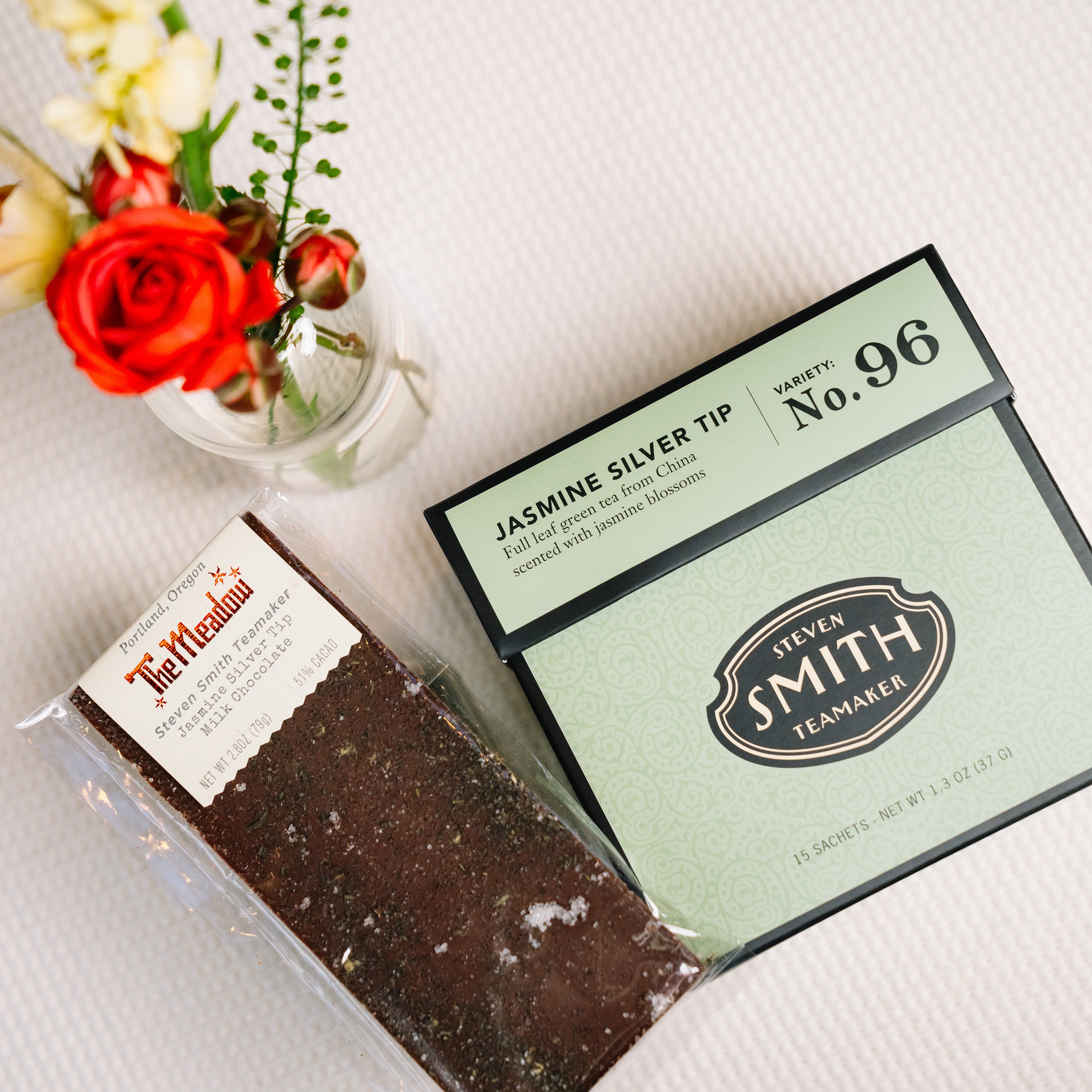 The Meadow Jasmine Silver Tea chocolate bar beside box of Jasmine Silver Tea green tea on a white cloth.