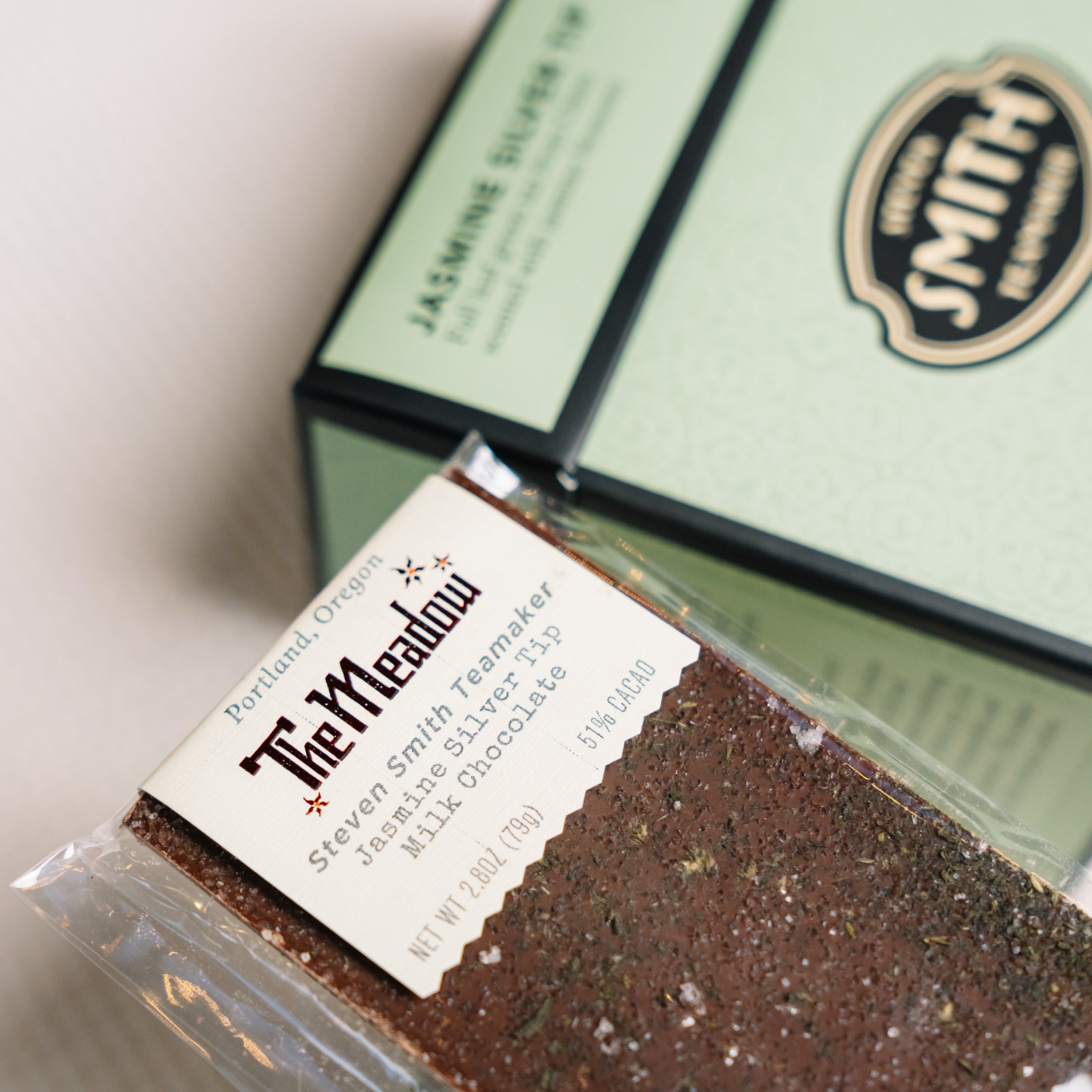 Close up on the Meadow Jasmine Silver Tea chocolate bar with box of Jasmine Silver Tea green tea in background.