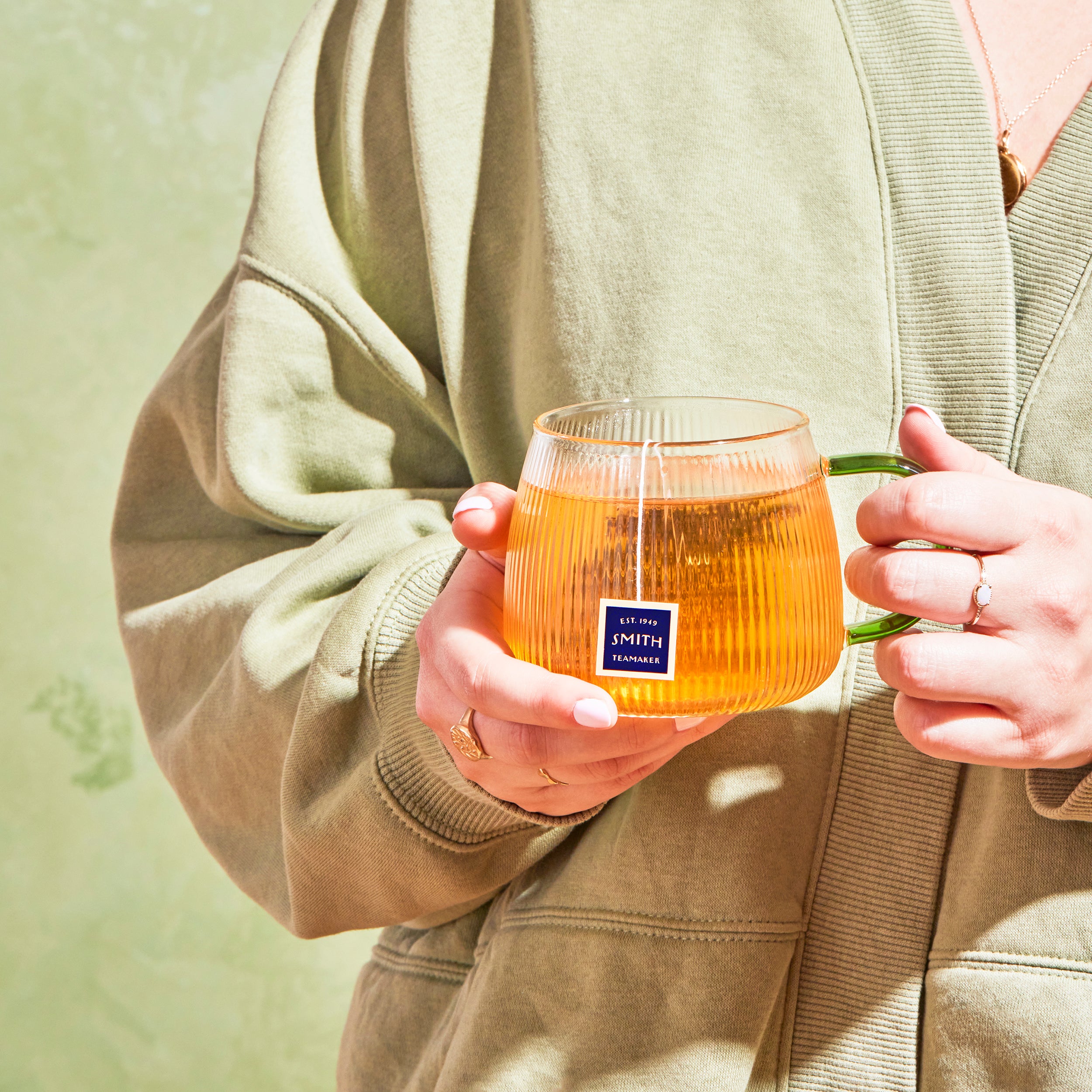 Glass cup of brewed tea with a Smith teabag in the cup held by a person in a pale green sweater.