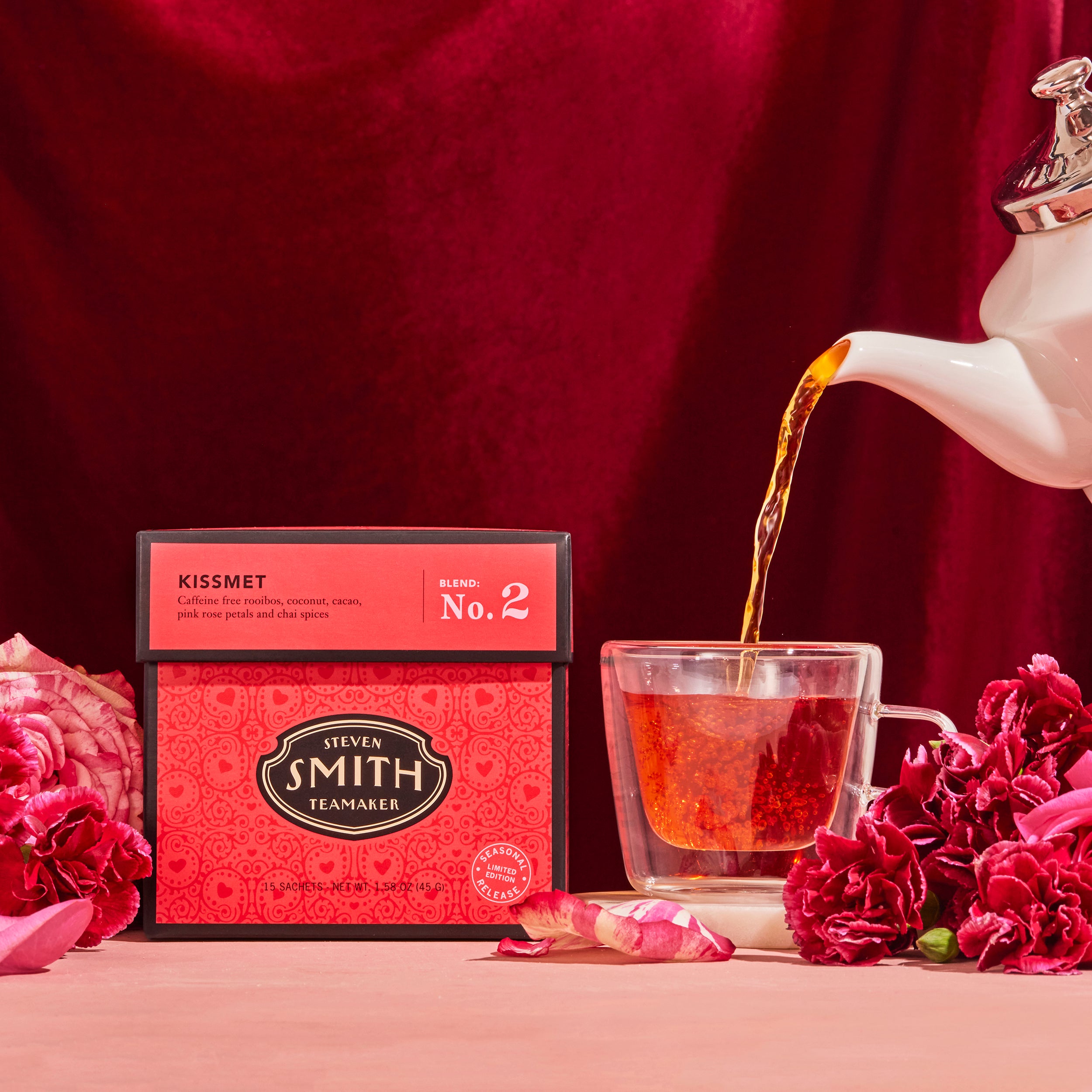 Deep pink box of Kissmet tea next to a glass teacup being filled with tea.