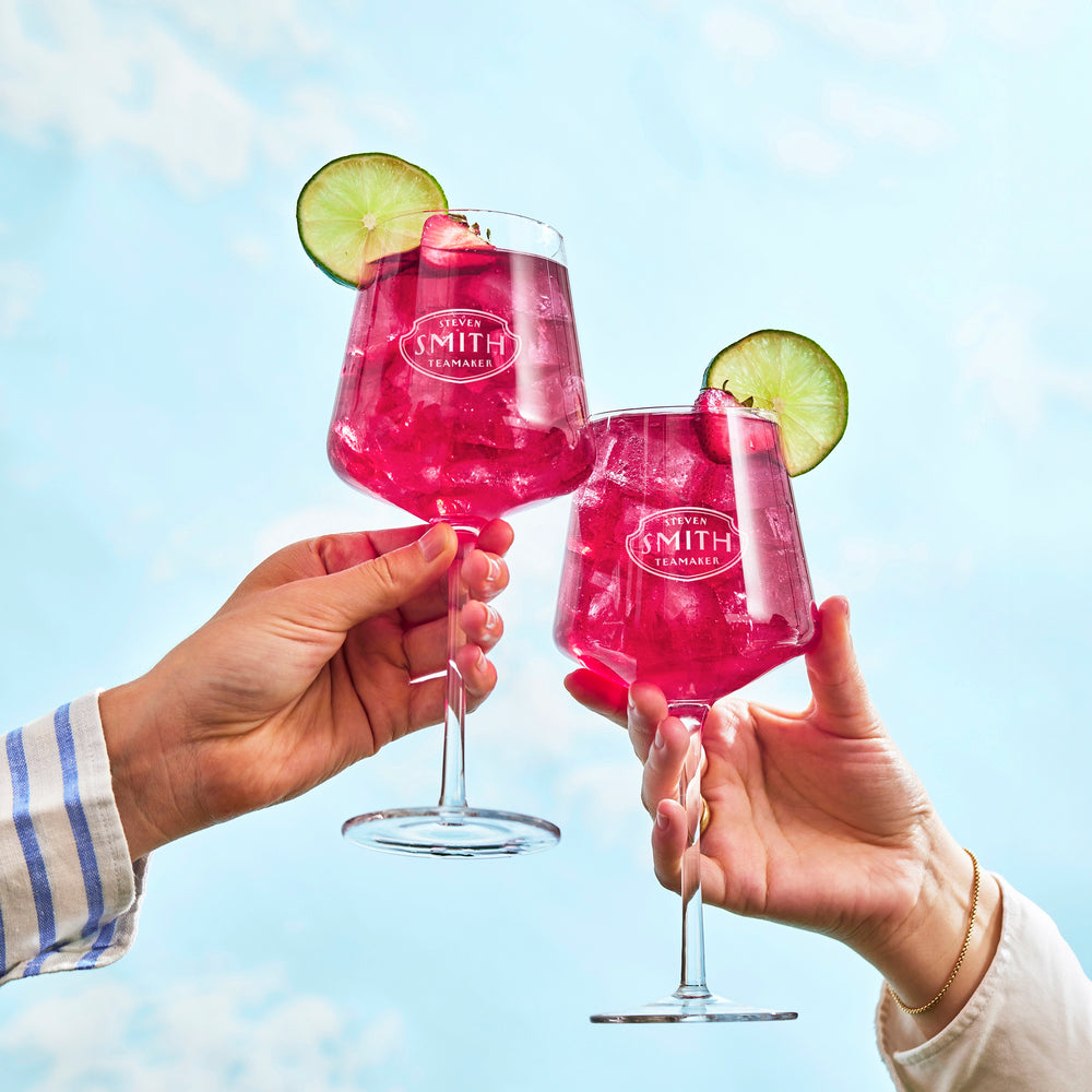 Two glasses of Lime Bramble Iced Tea in wine glasses held up for a cheers.