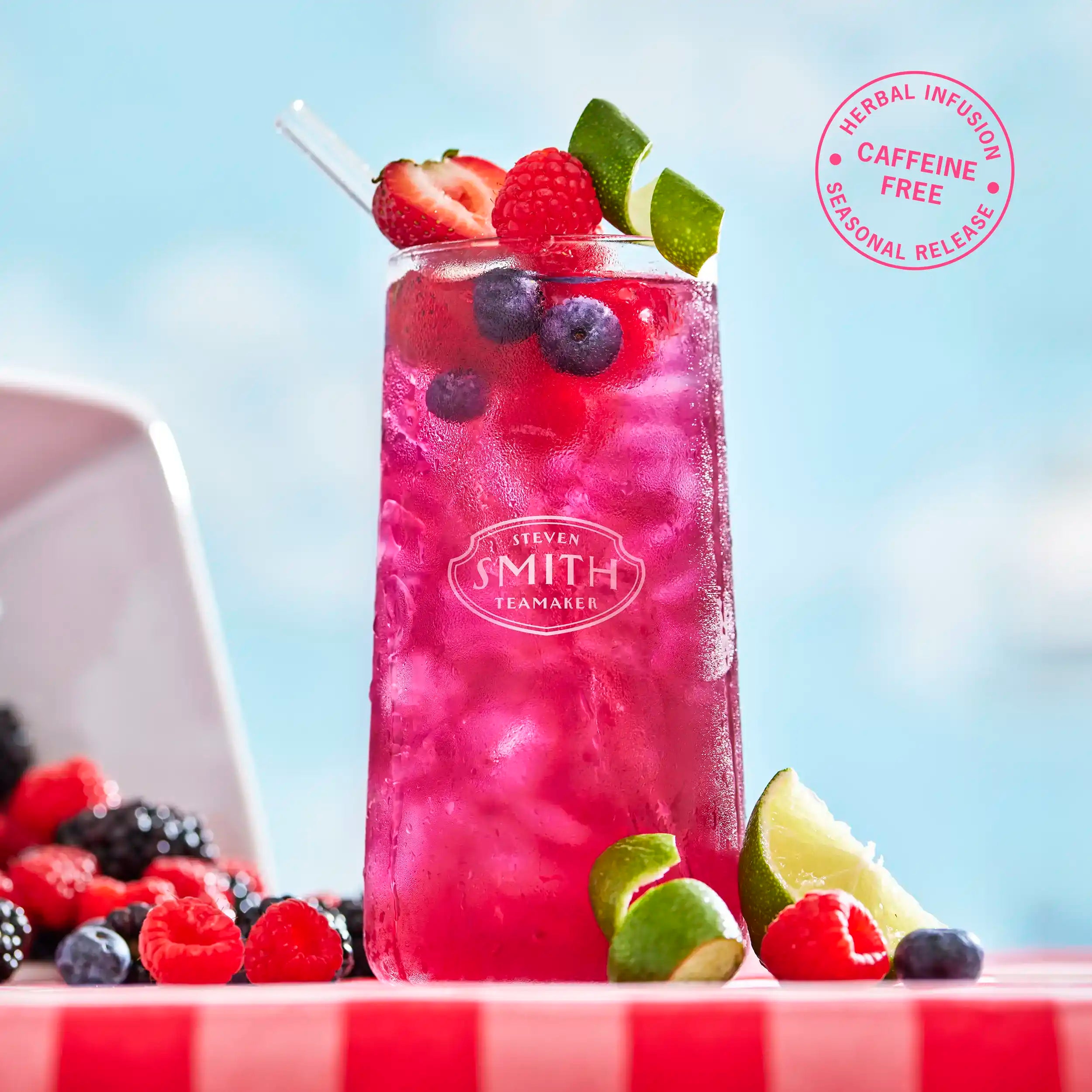 Glass of Lime Bramble Iced Tea on a picnic table garnished with fresh berries and lime.
