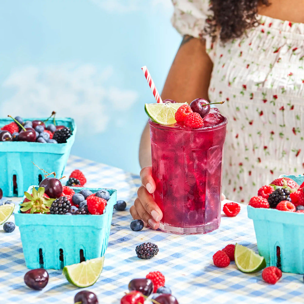 Large glass of Lime Bramble Iced Tea on a picnic table garnished with fresh berries and lime.