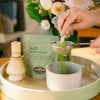 Matcha Latte Mix being sifted into a matcha bowl in a kitchen setting.