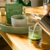 Glass cup filled halfway with matcha being topped with frothed milk in a kitchen setting.