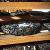 Wooden rack with aging Nan Nuo Shan Pu-erh cakes lining the shelves in Yunnan, China.