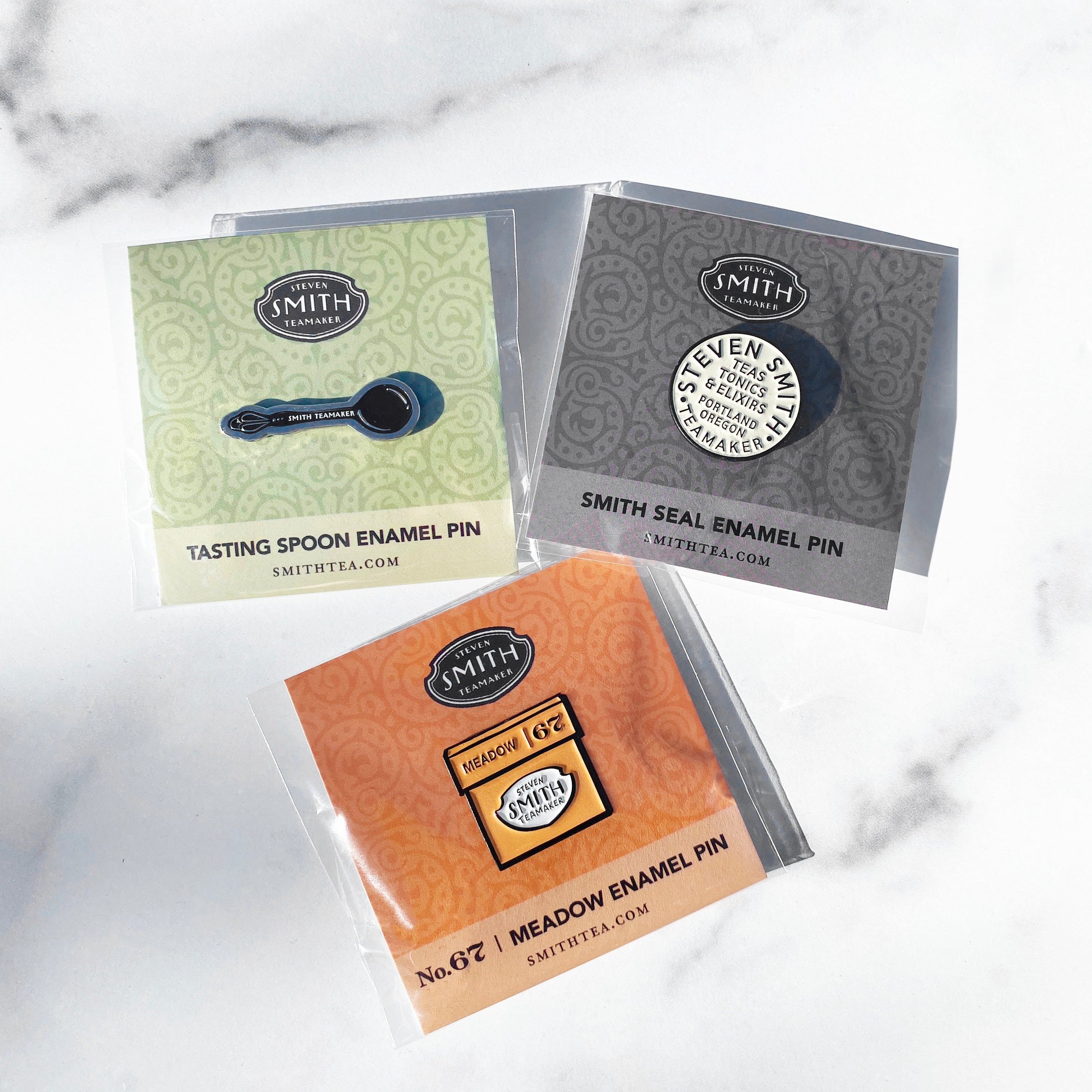 Tasting Spoon, Smith Seal and Meadow Carton enamel pins individually wrapped shown as a trio.