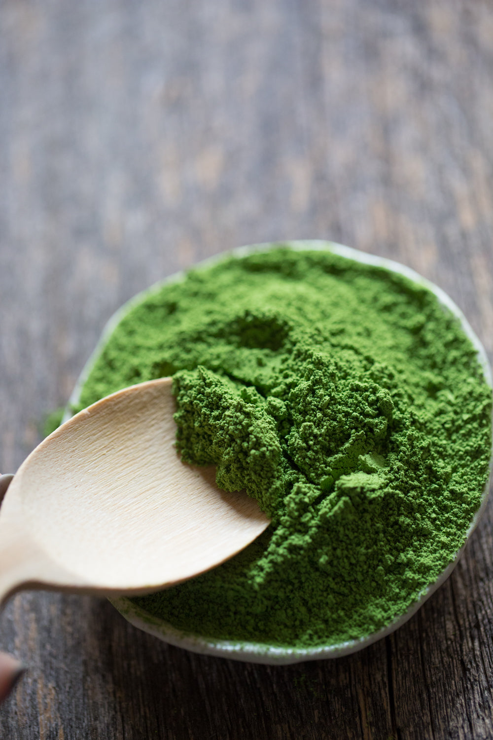 Ceramic bowl of loose matcha powder with a wooden spoon.