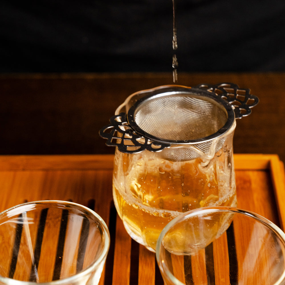 Glass teacup filled with brewed Tian Men Shan Sheng Pu-erh to show golden color of the liquor.