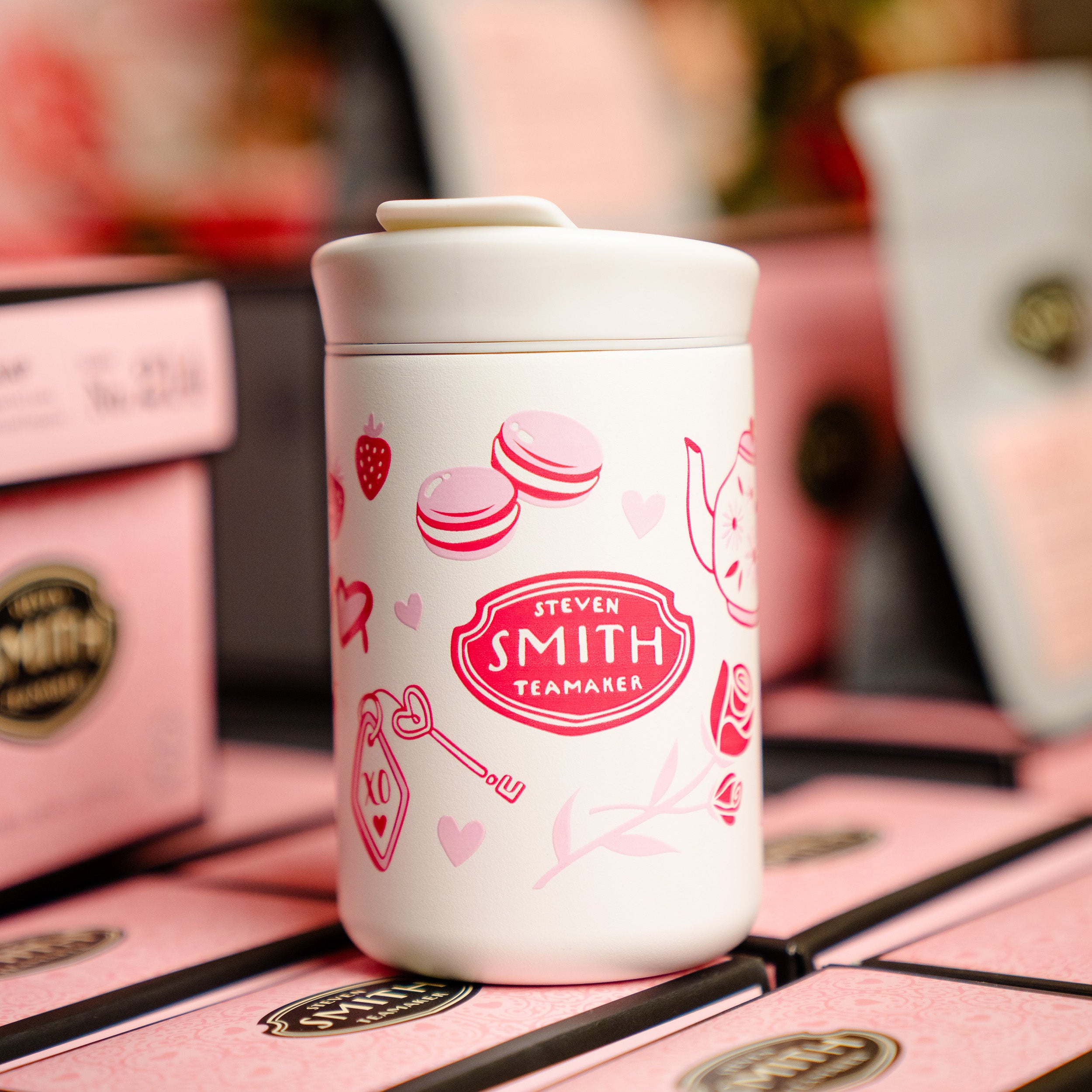 Small white beverage tumbler with a flip lid and pink Valentine's Day design with Smith logo in the middle placed on boxes of tea.