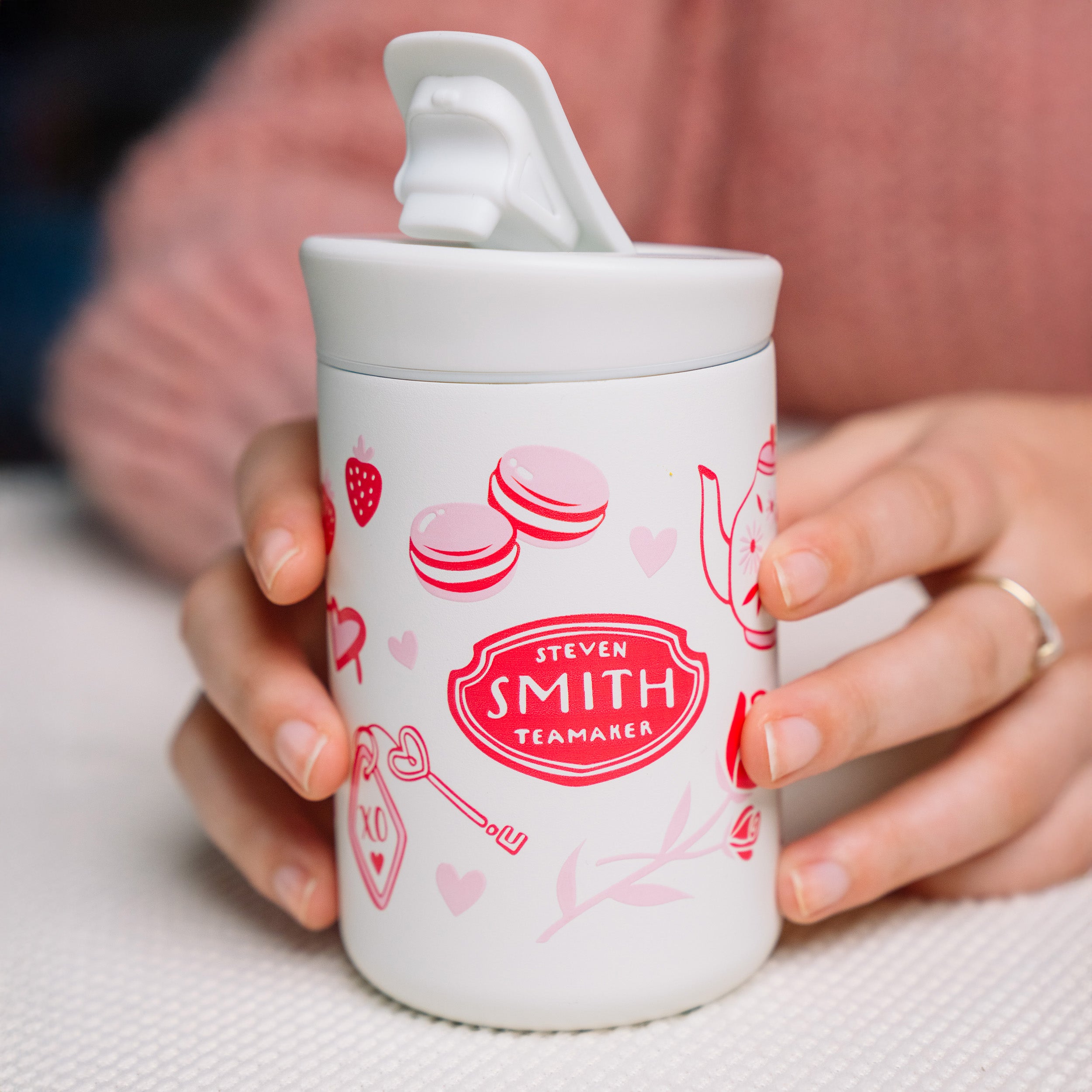 Small white beverage tumbler with a flip lid and pink Valentine's Day design with Smith logo in the middle.